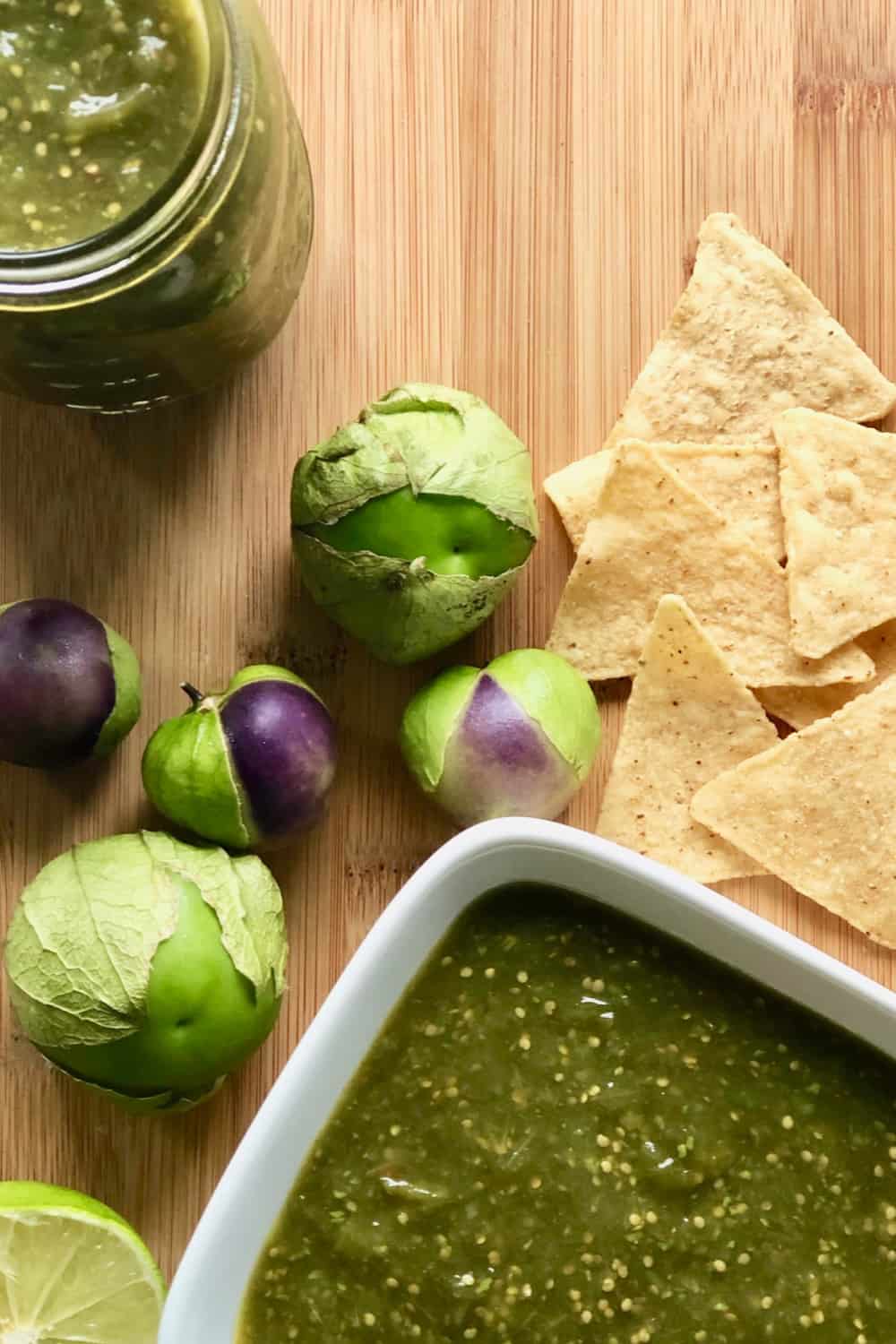 jar and bowl of salsa on cutting board with tomatillos and chips