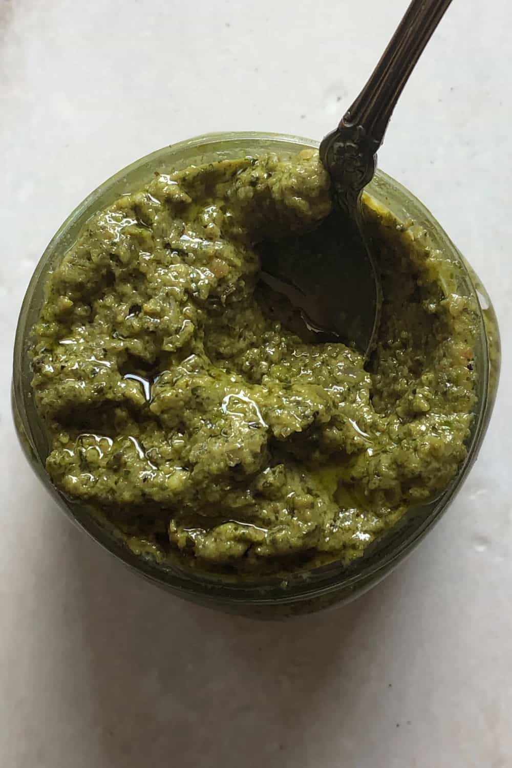 jar of pesto with a spoon resting on a table
