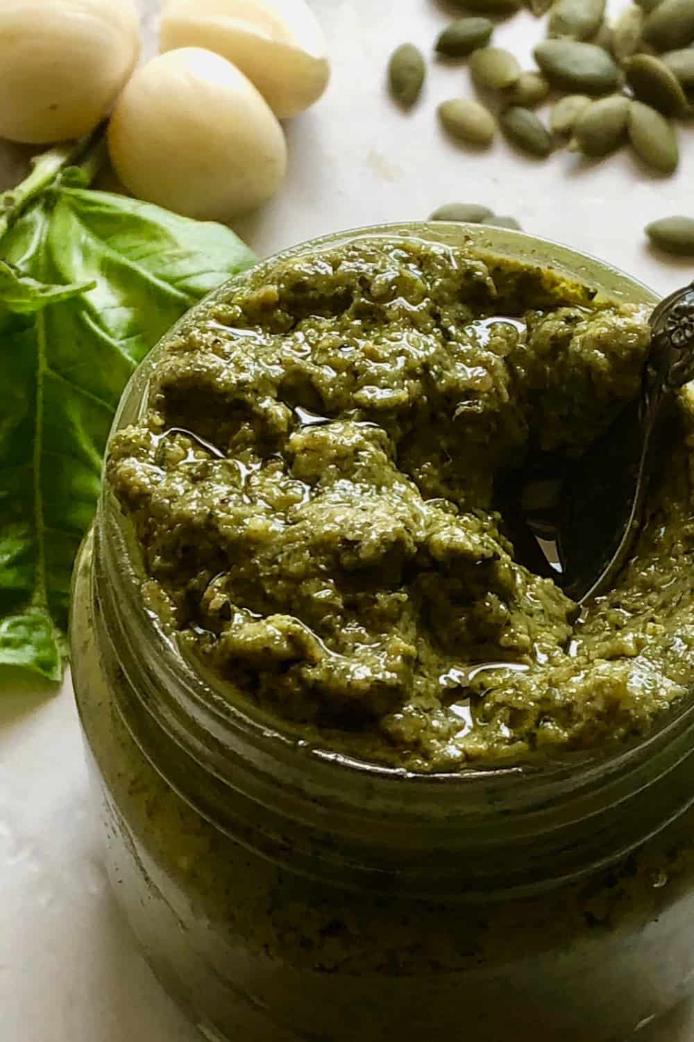 vegan pesto in a jar with basil. garlic and pumpkin seeds in the background