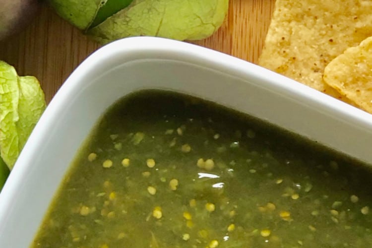 bowl of salsa verde on cutting board with tomatillos and chips