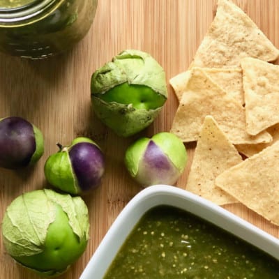 bowl of salsa verde on cutting board with tomatillos and chips