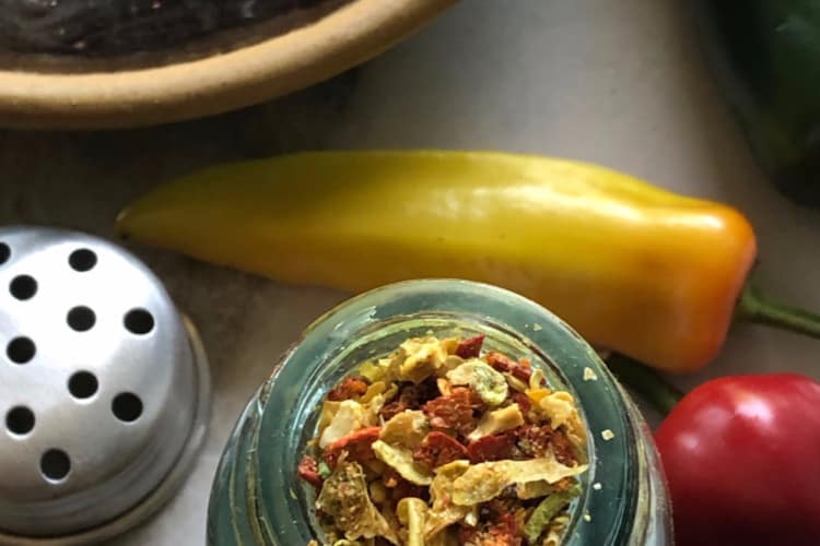 jar and bowl of hot pepper flakes with fresh peppers on a counter